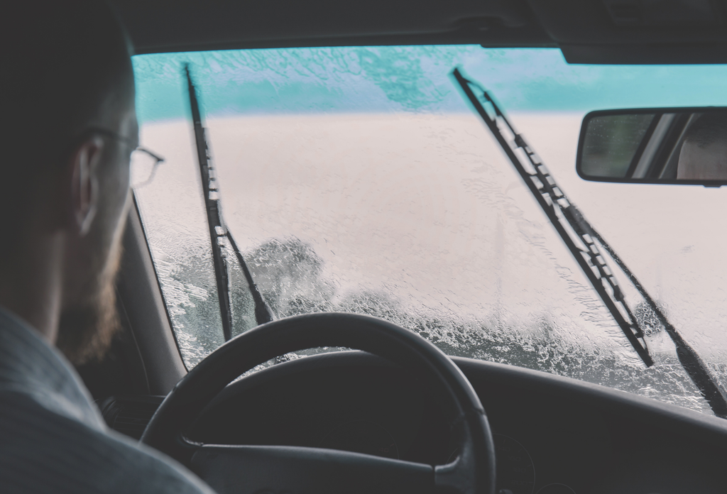 A driver attempting to keep their windshield clear while driving in freezing rain conditions.