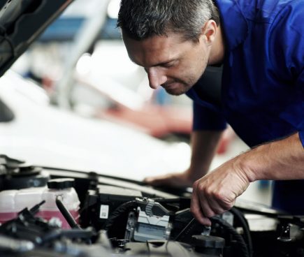 Automotive mechanic inspecting car engine inside repair shop